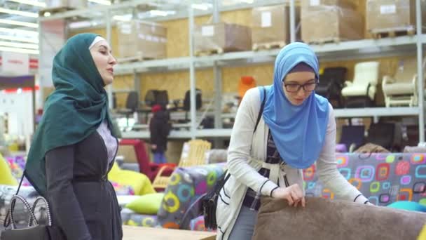 Δύο νέοι μουσουλμάνες γυναίκες επιλέγουν έναν καναπέ σε ένα κατάστημα επίπλων — Αρχείο Βίντεο