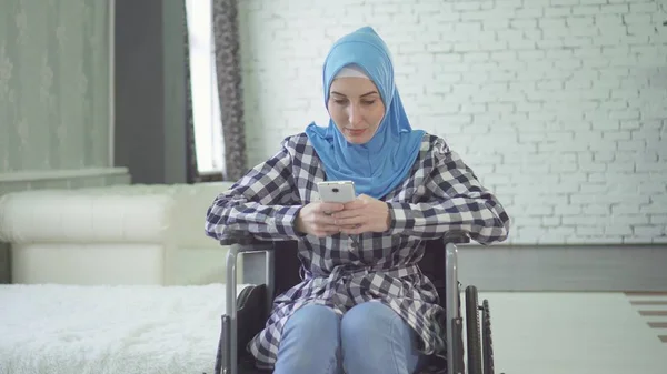 Wanita muda yang cantik di hijab orang cacat tersenyum, kursi roda, di apartemen Stok Foto Bebas Royalti