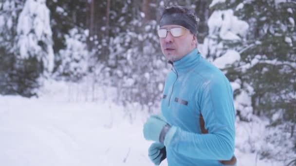 Porträt eines 40-jährigen Mannes, der durch den Winterwald läuft — Stockvideo