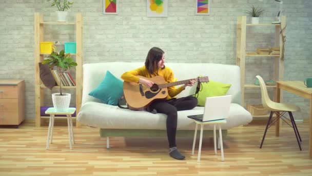 Молода жінка грає на гітарі, навчається в інтернеті, в сучасних квартирах — стокове відео