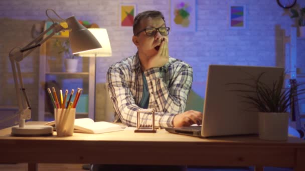 Ο νεαρός άντρας λείπει καθισμένος στο φορητό υπολογιστή τη νύχτα — Αρχείο Βίντεο
