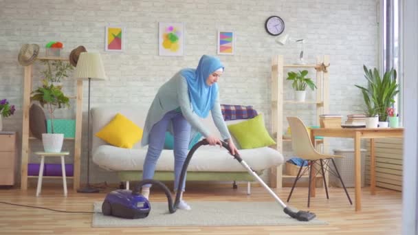 Мусульманка в хиджабе убирает дом пылесосом — стоковое видео