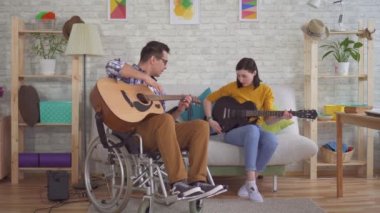 Tekerlekli sandalye gitarist genç özürlü adam gitar oynamak için bir kız öğretir