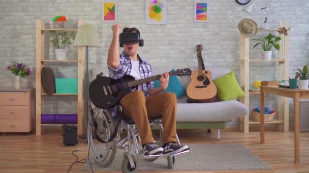 Junger Mann behinderter Musiker im Rollstuhl und Virtual-Reality-Brille spielt Gitarre — Stockvideo