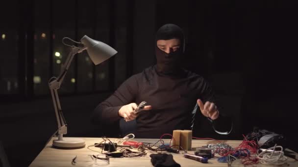 Портрет террориста в маске балаклавы, делающего бомбу ночью — стоковое видео