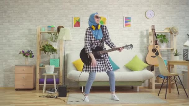 Alegre musulmana joven en hijab toca la guitarra electro en casa — Vídeos de Stock