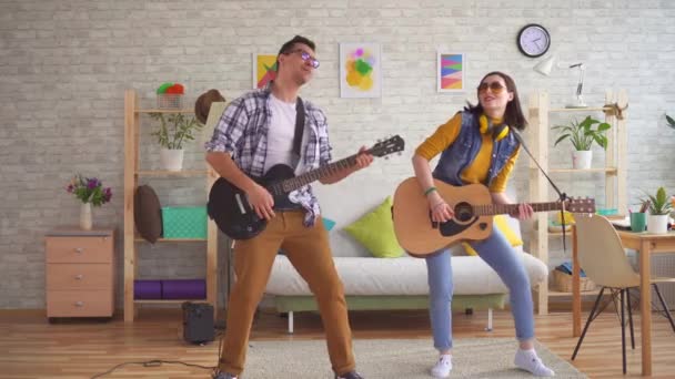 Joven mujer y un hombre joven emocionalmente tocar guitarras y bailar — Vídeos de Stock