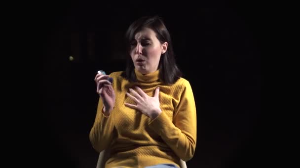 Cara joven mujer está enferma de asma, utilizando un inhalador asmático, primer plano sobre un fondo negro — Vídeo de stock