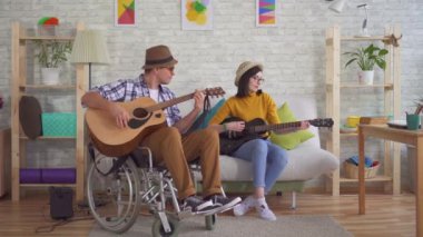 Bir tekerlekli sandalye gitarist ve genç kadın gitar oynarken genç özürlü adam