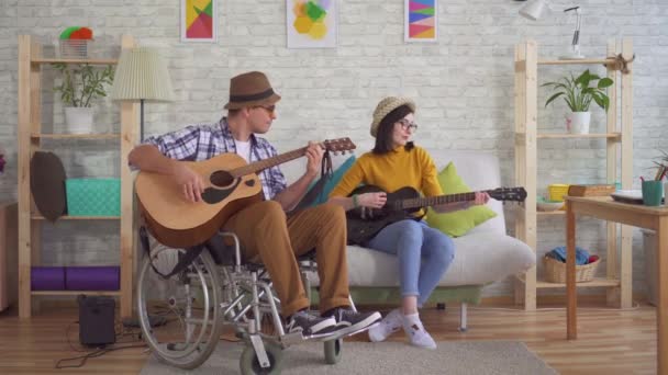 坐在轮椅吉他手和年轻女子弹奏吉他的年轻残疾男子 — 图库视频影像