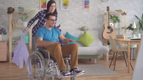 Jonge vrouw helpt een gehandicapte persoon in een rolstoel te krijgen gekleed — Stockvideo