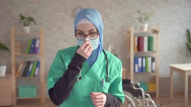 Портрет мусульманки в хиджабе доктор снимает повязку улыбаясь и глядя в камеру — стоковое видео