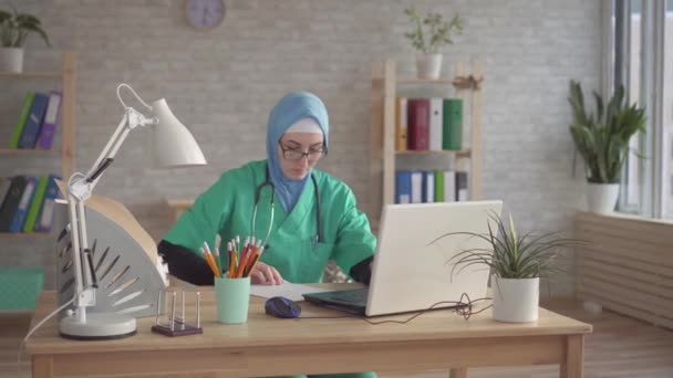 Портрет мусульманки в хіджабі лікар на робочому місці в сучасній клініці — стокове відео