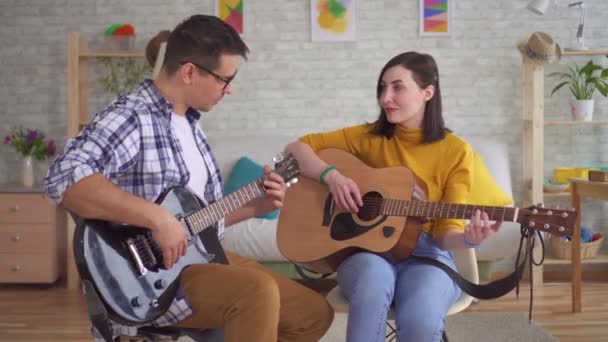 若い男ギタリストは、ギターを弾くために若い女性を教えます — ストック動画