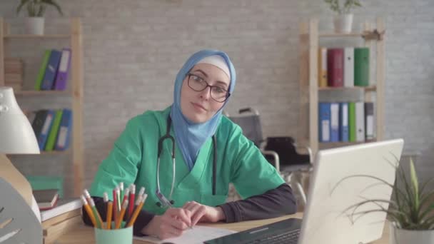 Primo piano del medico musulmano in hijab sul posto di lavoro per un computer portatile — Video Stock