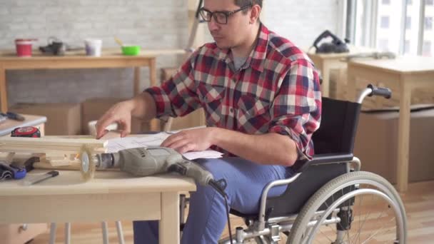 Portret van een jonge gehandicapte in een rolstoel met een elektrische boor die zich bezighoudt met de montage van meubilair — Stockvideo