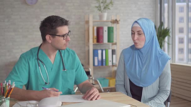 Портрет молодой мусульманки в хиджабе на приеме у врача мужчины — стоковое видео