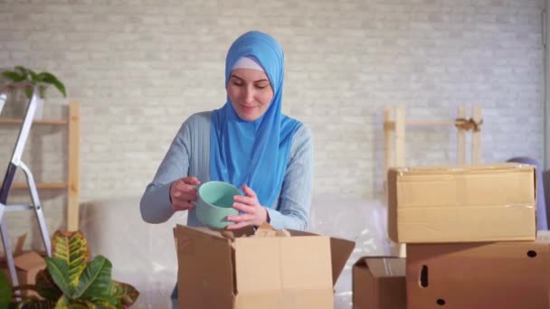 Mujer musulmana desempaca una caja de platos durante el movimiento y encuentra daño — Vídeo de stock