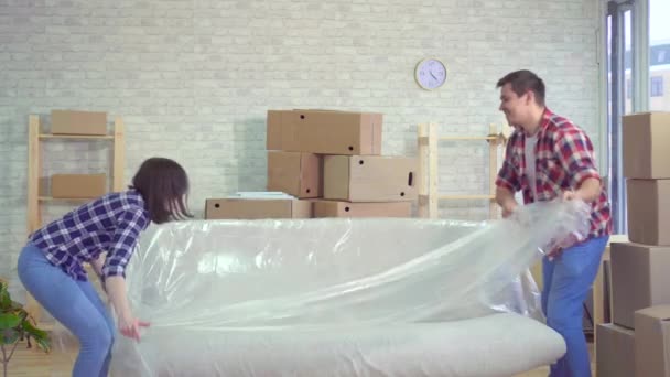 Young married couple remove the oilcloth from the sofa after moving — Stock Video