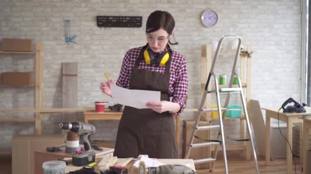 Wanita pekerja muda profesional tukang kayu dengan diagram di tangan membuat pengukuran menggunakan ukuran pita — Stok Video