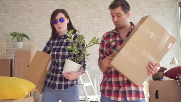 Веселая молодая пара входит в новый дом, танцует и веселится с коробками в руках — стоковое видео