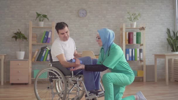 Verpleegster Moslimvrouw in een hijab helpt bij de rehabilitatie van personen met een handicap in een rolstoel — Stockvideo