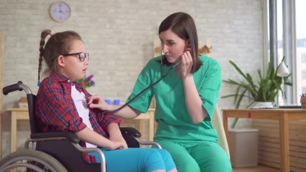Терапевт и ребенок в инвалидном кресле использование стетоскопа — стоковое видео
