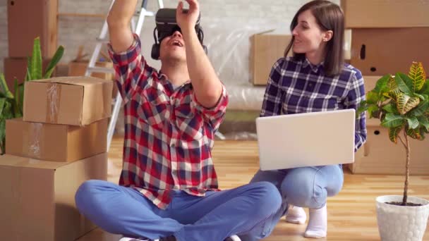 Mujer con un portátil muestra a un hombre en gafas de realidad virtual el proyecto de un nuevo apartamento — Vídeo de stock