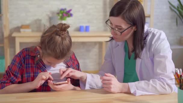 Doctor psychologist teaches an autistic child to use a smartphone — Stock Video