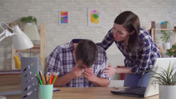 Young man in glasses sitting at laptop coughs with blood his wife supports — Stock Video