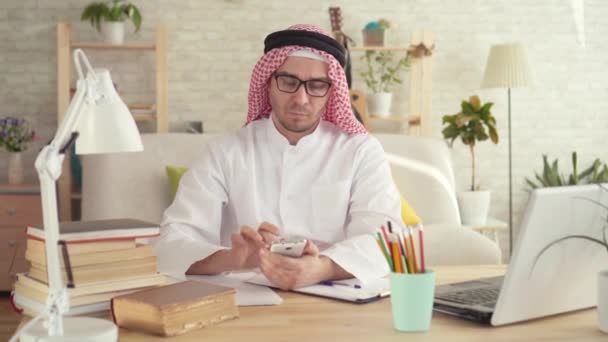 Homem árabe sentado à mesa e ele usa um smartphone — Vídeo de Stock