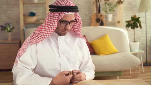 Arab man sitting at the table holding a rosary in his hands and reading a prayer — Stock Video