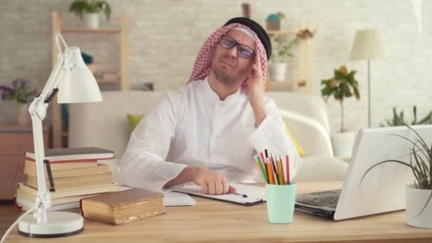 Hombre árabe sentado a la mesa con dolor de cabeza — Vídeos de Stock