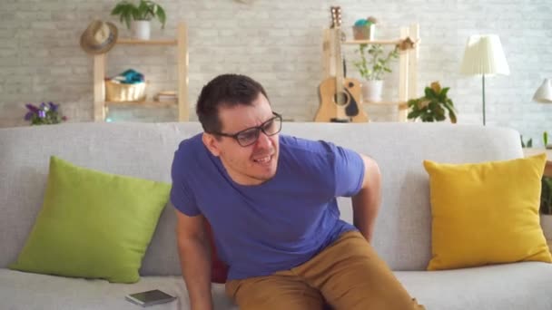 Портрет нездоровий чоловік відчуває дискомфорт від геморою, сидячи на дивані — стокове відео