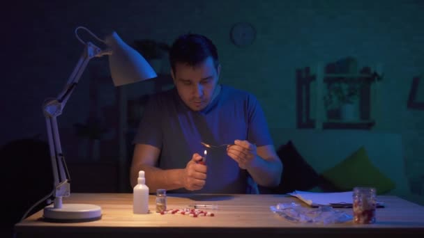 Hombre adicto en un cuarto oscuro en una mesa preparándose para la inyección — Vídeos de Stock