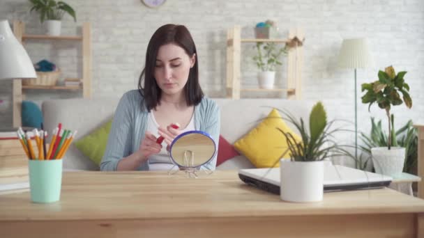 Young woman smears chapped lips lipstick sitting in front of mirror — Stock Video