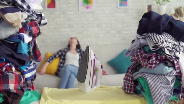 Portrét unavené ženy v domácnosti na pozadí hromádek šatů — Stock video