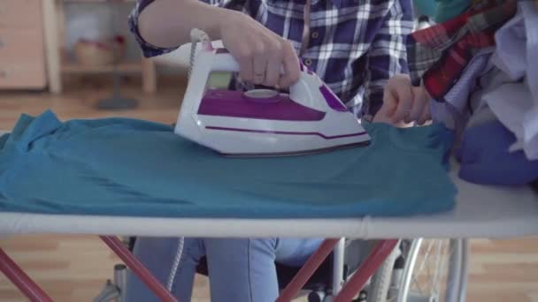 Schöne behinderte Frau im Rollstuhl beim Hausaufgabenmachen, Bügeln von Kleidung — Stockvideo