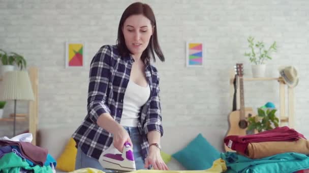 Fröhliche junge Frau im karierten Hemd gebügeltes Leinenbügeleisen zu Hause, tanzend aus nächster Nähe — Stockvideo