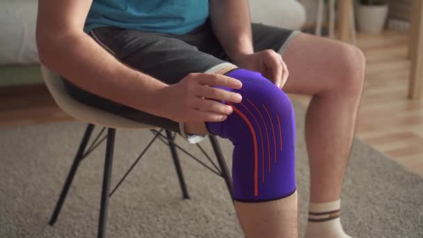 Nahaufnahme eines männlichen Athleten, der nach einer Verletzung auf einem Stuhl sitzt und einen Verband am Knie zieht — Stockvideo
