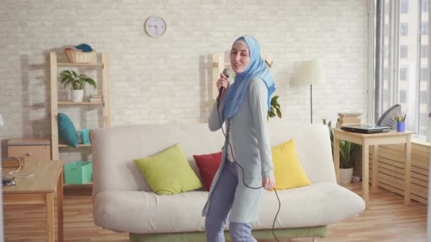 Cheerful expressive Muslim girl in hijab in karaoke microphone at home — Stock Video