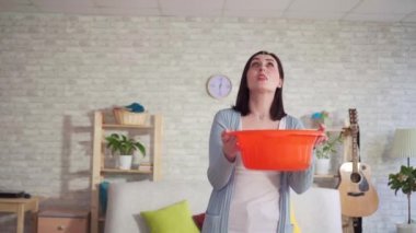 Şaşkın genç kadın tavandan su damlaları yakalar ve kameraya bakar