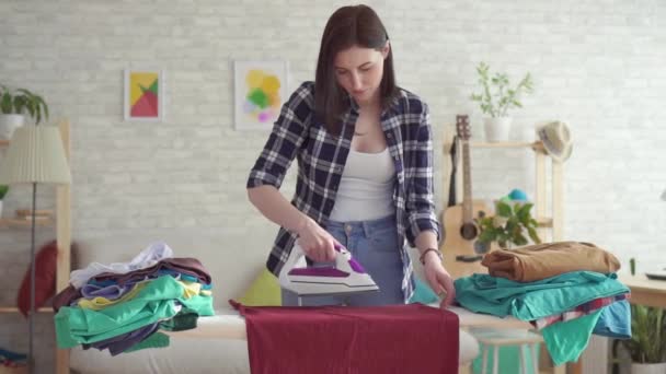Linda mujer joven en camisa a cuadros Planchado Lavandería plancha en casa — Vídeos de Stock