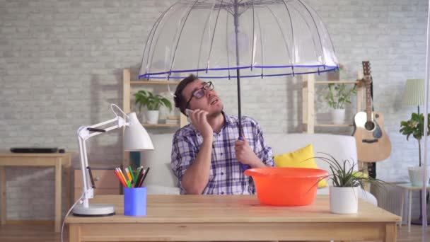 Homem debaixo de um guarda-chuva no telefone relatórios sobre a inundação em seu apartamento — Vídeo de Stock