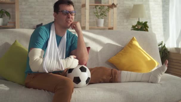 Portrait sad injured athlete sitting on the couch with a soccer ball — Stock Video