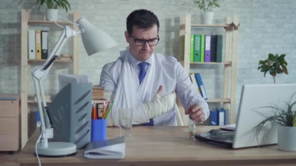 Man kantoormedewerker met gebroken arm drinken geneeskunde — Stockvideo