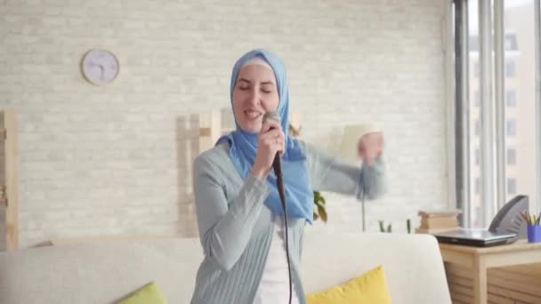 Alegre expresiva chica musulmana en hijab en el micrófono de karaoke en casa — Vídeos de Stock