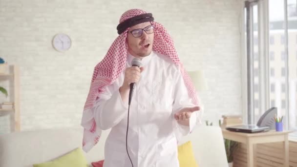 Veselý arabský muž v tradičním oblečení, zpívající v karaoke mikrofonu doma — Stock video