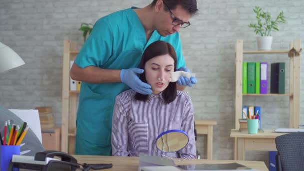 Пластический хирург снимает повязку с лица женщины после операции — стоковое видео