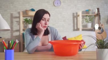 Umutsuz kadın masaya oturur ve kova içine tavandan damlar su olarak izler